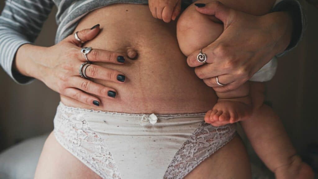 Tatuaggio di una mamma con il suo bambino sul ventre, simbolo di connessione e cura nel puerperio.
