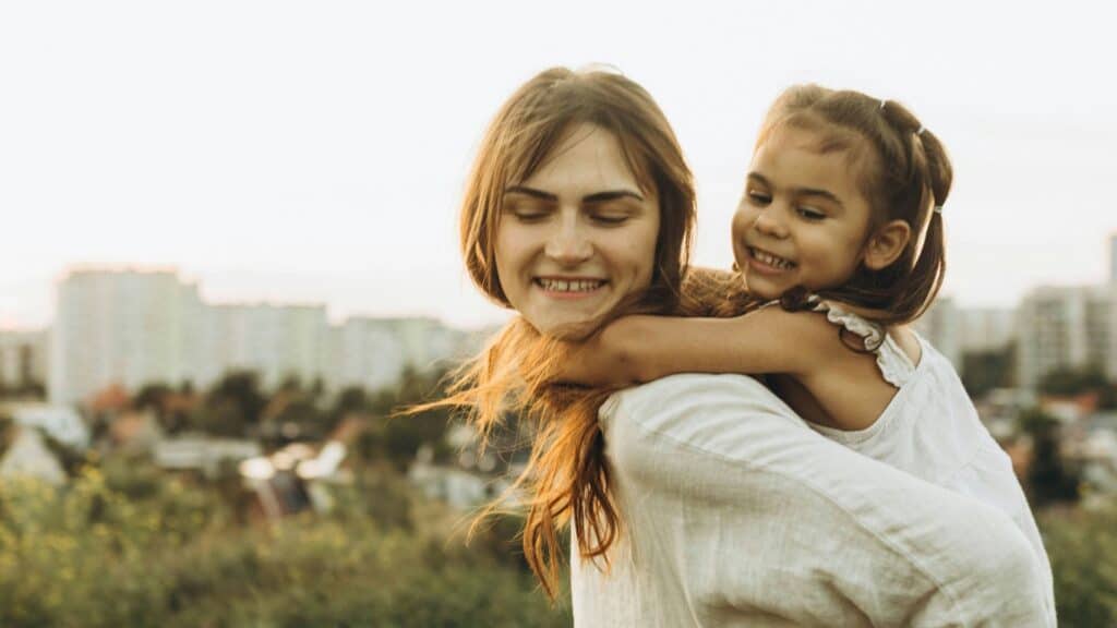 Madre che tiene la figlia sulle spalle al tramonto