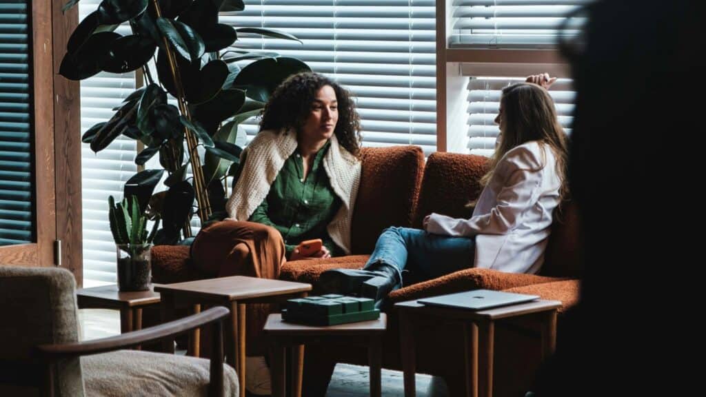 Due donne sedute su un divano che conversano in un ambiente luminoso