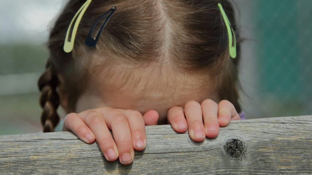 Bambina che nasconde il viso dietro una staccionata di legno