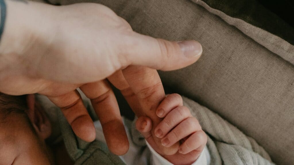 Mano di una mamma stretta dalla manina del neonato che dorme