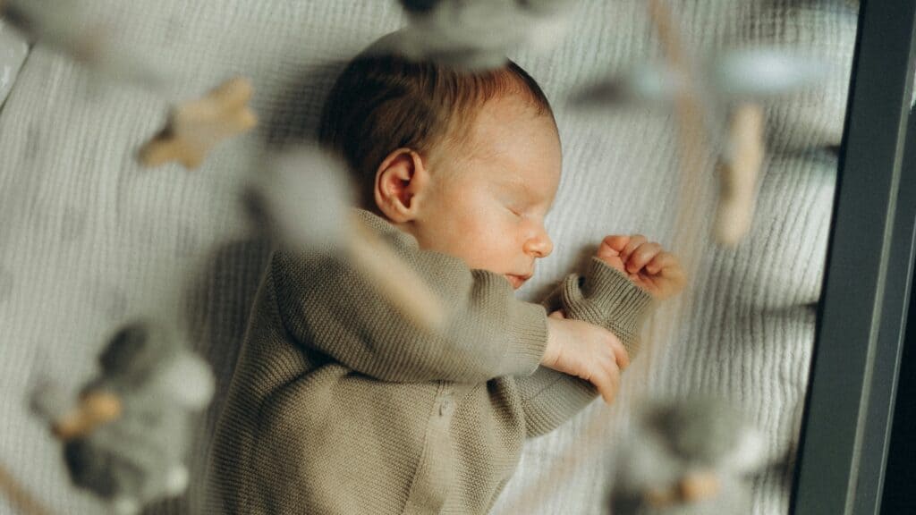 Neonato che dorme sulla schiena nella culla, sotto una giostrina: lo sviluppo del sonno del bambino